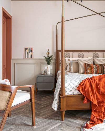 Bedroom with wooden four-poster bed, orange throw, cane chair and herringbone floor