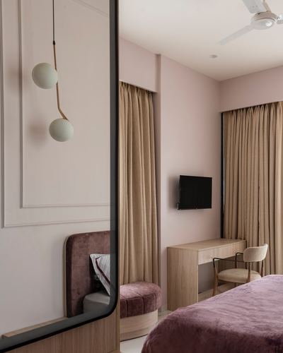 Pink-toned bedroom with mauve velvet bed, wooden desk, and a double-globe pendant light reflected in a mirror