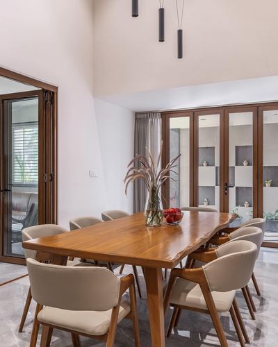 Dining room with live-edge wood table, cream chairs, and cylindrical pendant lights under double-height ceiling