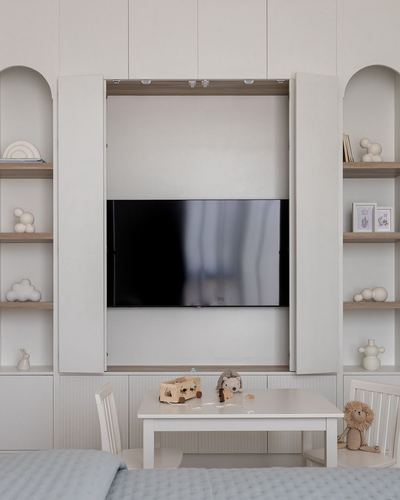 Symmetrical built-in wall with arched shelves and cabinet doors open to reveal a hidden television, child's table below.