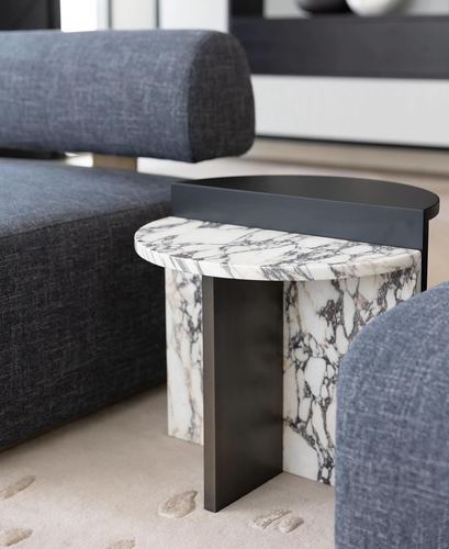 Close-up of a marble and dark metal side table beside a grey upholstered sofa