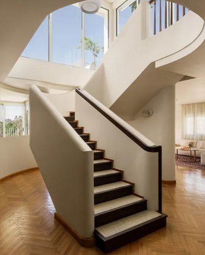 Curved white staircase with dark wood treads rising through double-height foyer with herringbone floor