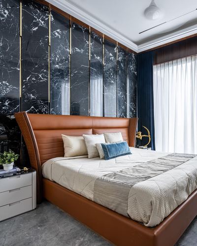 Bedroom with black stone panel wall, brass strips, and tan leather bed frame