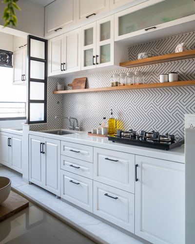 White modular kitchen with patterned geometric backsplash, open wood shelves, and black gas hob
