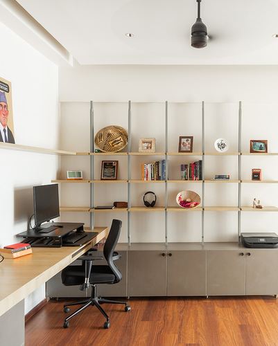 Home study with modular open shelving, wooden desk, black office chair and wood flooring