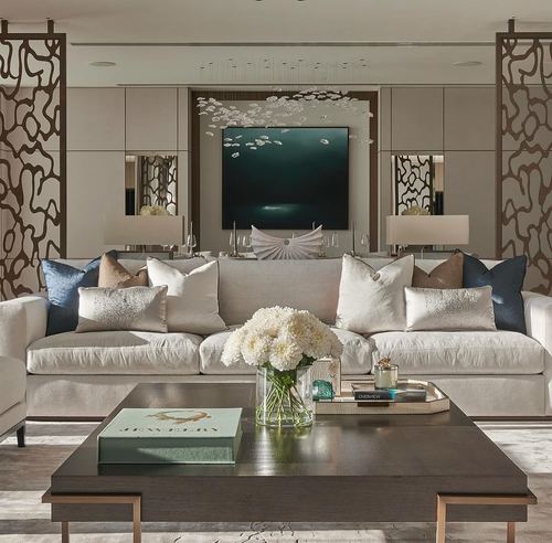 Cream sectional sofa faces a dark teal artwork flanked by carved metal screens and mirrored side tables