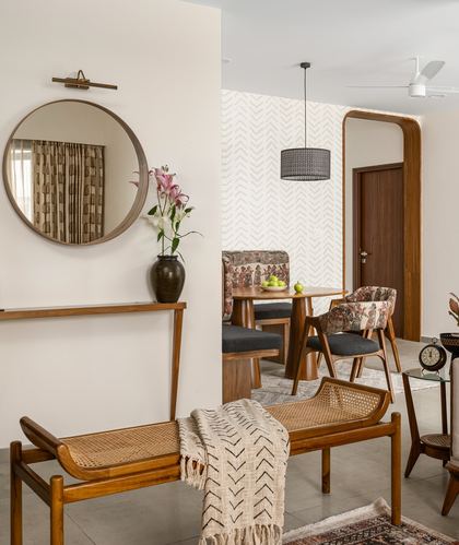 Foyer with round mirror and cane bench opening through arched doorway to dining area