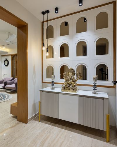 Foyer with arched mirrored panel wall, brass Ganesh idol on console, pendant bulbs, wood-framed archway to living room