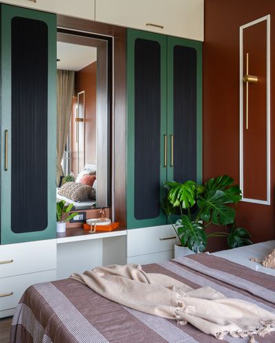 Green fluted wardrobe doors flank a mirrored dressing nook beside a terracotta wall in a styled bedroom