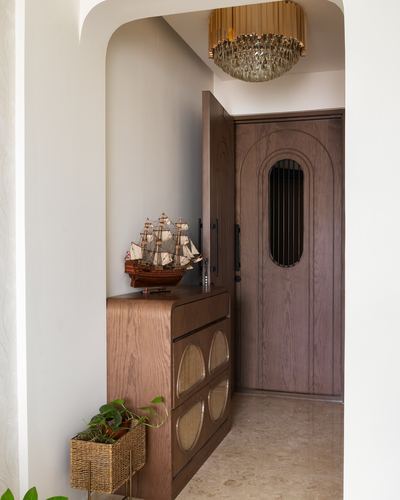 Arched foyer with wood door, cane-front cabinet, model ship, and glass chandelier above