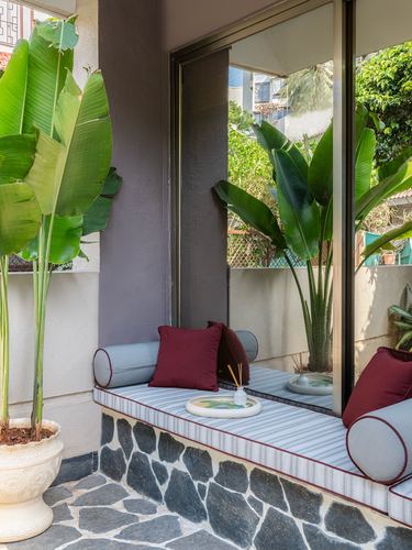 Balcony window seat with striped cushion, maroon bolsters, stone base, and large banana leaf plant