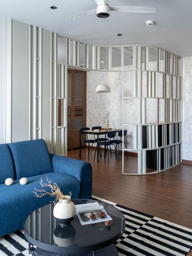Living room with blue sofa, curved slatted partition, and dining area beyond on wood flooring