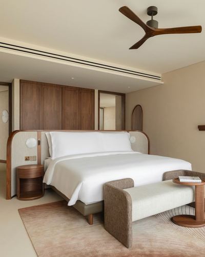 Warm-toned bedroom with curved wood headboard, wooden ceiling fan, and bench at foot of bed