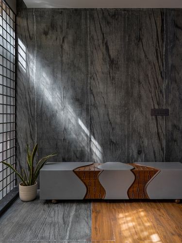 Grey stone-clad wall with sunbeam falling on a sideboard with a carved wave-shaped wooden inset