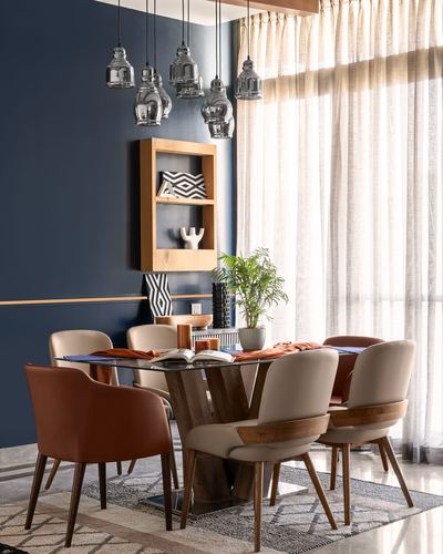 Dining room with glass-top table, mixed upholstered chairs, and cluster pendant lights against navy wall