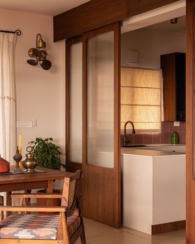 Dining table beside a wood-framed frosted glass sliding door opening into a warm-lit kitchen