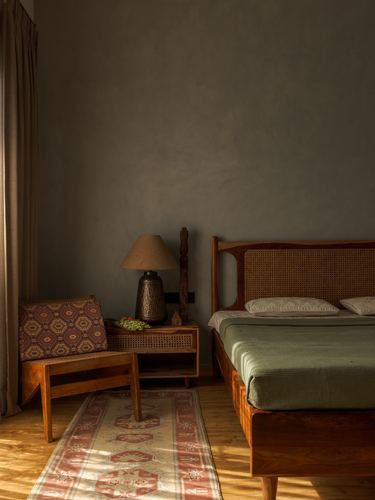 Warm-lit bedroom with cane headboard bed, wooden armchair, patterned rug on wood floor