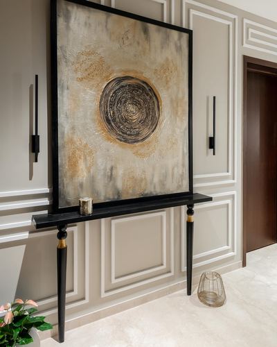 Foyer console table beneath a large abstract painting flanked by wall sconces and molded panels