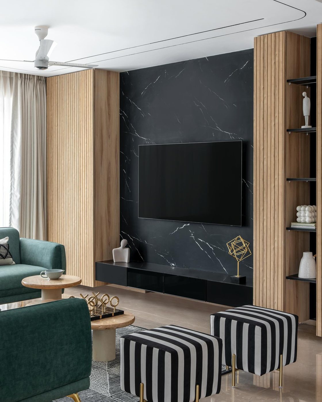 Living room with black stone tv wall, fluted wood panels, green sofas and striped ottomans