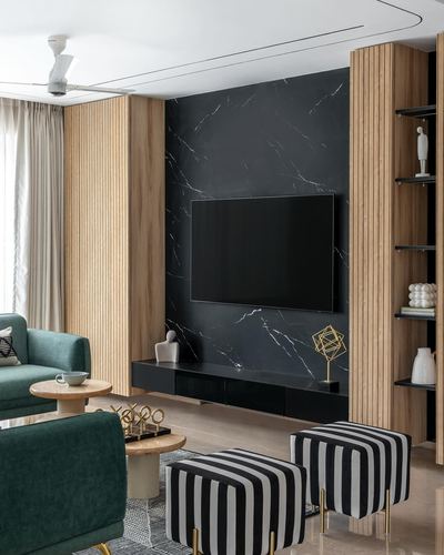 Living room with black stone tv wall, fluted wood panels, green sofas and striped ottomans