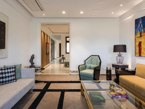 Art deco living room with mustard sofa, teal curved armchair, glass coffee table, and marble floor