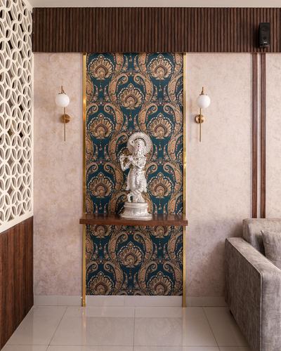 Pooja niche with deity statue against teal paisley wallpaper, flanked by brass sconces and jali screen