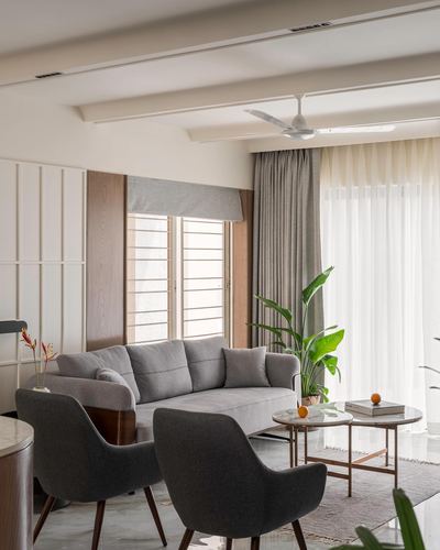 Grey sofa and armchairs around round marble coffee tables in a sunlit living room with sheer curtains