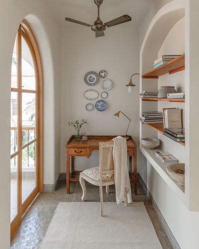 Small study nook with wooden desk, cane chair, arched shelving and display plates in a Goan home