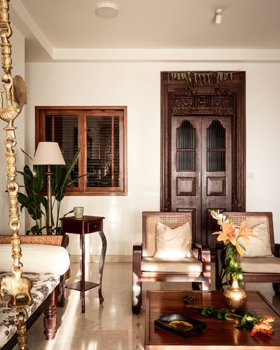 Traditional living room with carved wooden door, cane armchairs, and brass swing in a Bangalore heritage-style apartment