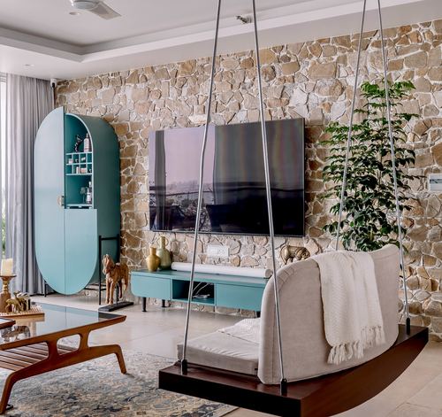 Living room with stacked stone accent wall, teal oval cabinet, and a hanging wooden swing seat facing a tv