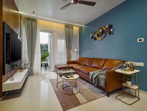 Living room with blue accent wall, tan leather sofa, gold-rimmed coffee tables, and balcony view