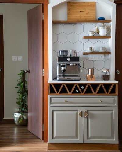 Arched coffee nook with hexagonal tile backsplash, espresso machine, and sage cabinetry beside open wooden door
