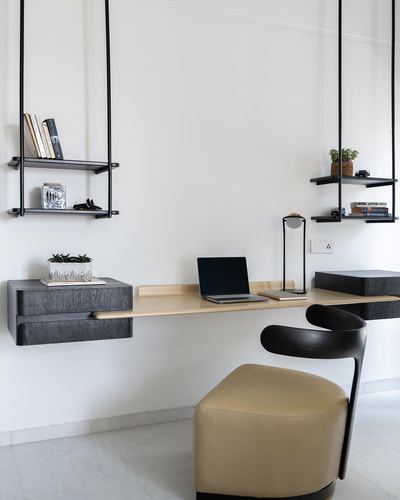 Wall-mounted study desk with suspended black shelves and a leather chair against a white wall