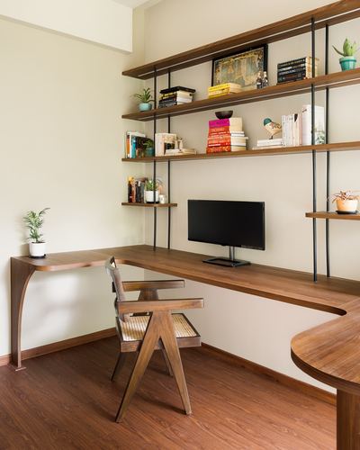 Wooden corner desk with cane chair beneath tall wood-and-metal shelving unit holding books and plants