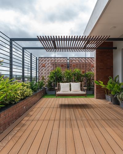 Rooftop terrace with wooden deck, hanging swing, terracotta jaali screen and greenery under overcast sky