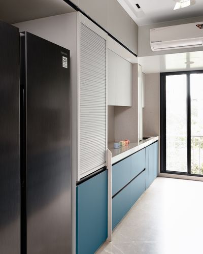 Modern galley kitchen with blue lower cabinets, white uppers, and a stainless refrigerator beside a balcony door.
