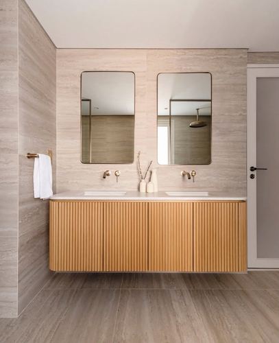 Floating fluted wood double vanity with two mirrors and brass fixtures against beige stone wall