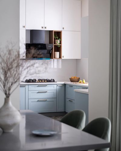Pale blue and white kitchen seen through foreground dining table with green velvet chairs