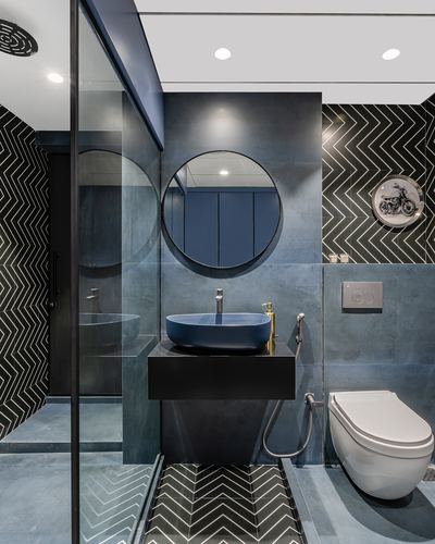 Modern bathroom with round mirror, dark vessel sink, chevron tile floor and glass shower partition