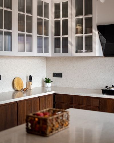Kitchen corner with fluted glass cabinets, stone countertop, wood base units, and wicker fruit basket in foreground.