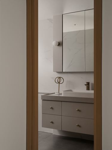 View through oak-framed doorway into bathroom with mirrored cabinet, vessel sink, and taupe drawers