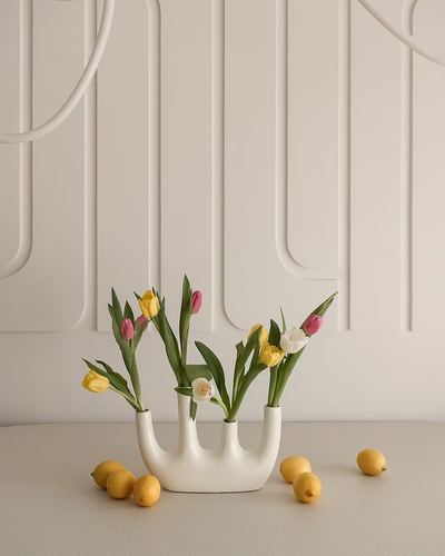 White multi-spout ceramic vase with tulips and lemons against a curved fluted plaster wall