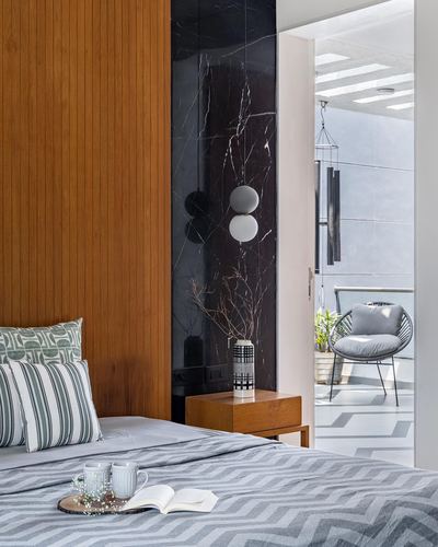 Bedroom with fluted wood headboard, marble accent wall, globe pendants, and view to balcony