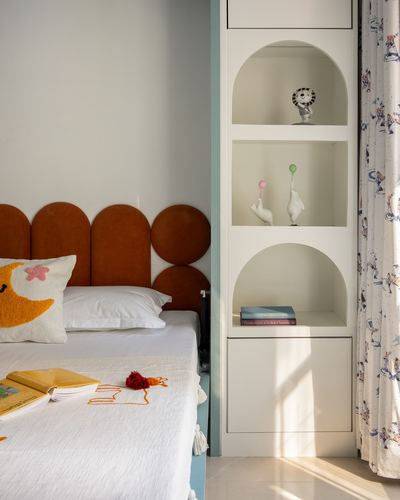 Kids bedroom corner with rust scalloped headboard and arched white shelving niches lit by daylight