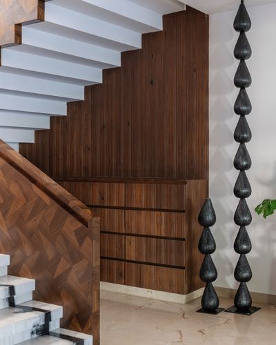 White cantilevered staircase beside ribbed wood wall with black teardrop floor sculptures