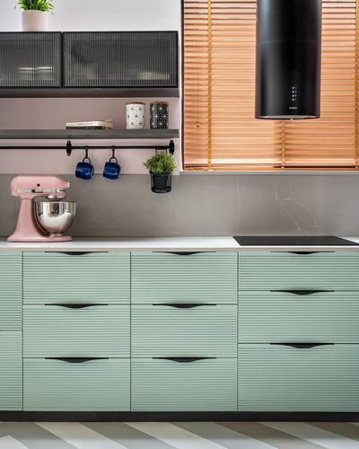 Mint green ribbed kitchen cabinets with black hood, pink stand mixer, and copper-toned blinds