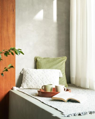 Window seat nook with green and white cushions, tray with mugs and an open book