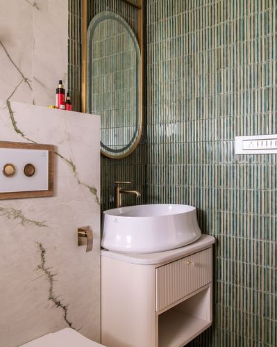 Bathroom corner with green fluted tile, oval brass mirror, and vessel sink on ivory marble vanity