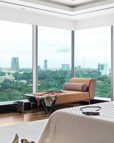 Camel leather chaise by corner floor-to-ceiling windows overlooking Bangalore skyline and park