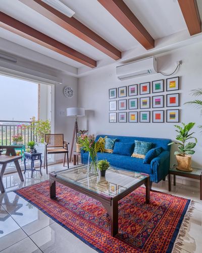 Living room with blue sofa, patterned rug, glass coffee table and colorful gallery wall, balcony beyond